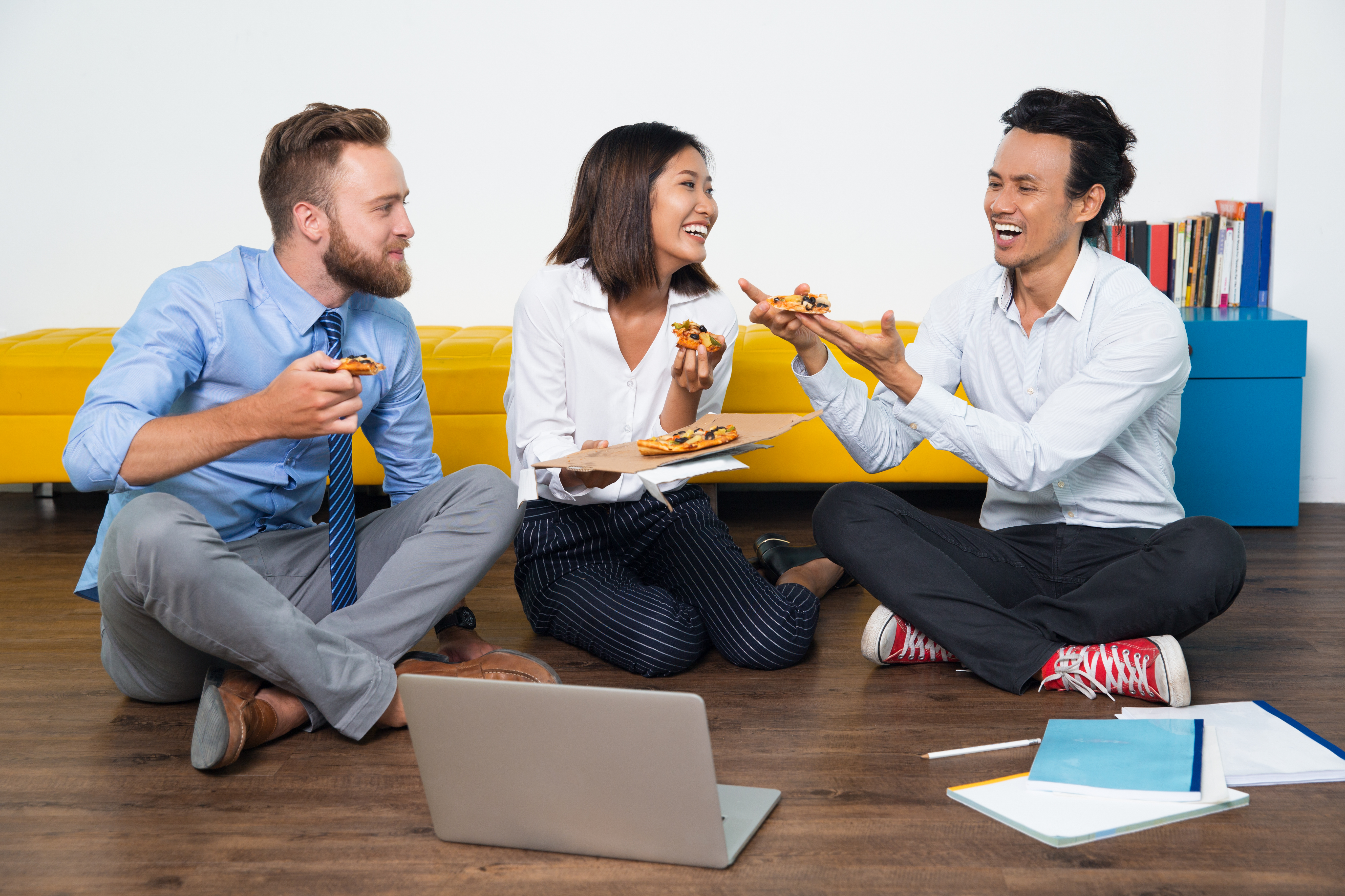 Happy colleagues sitting on floor and eating pizza