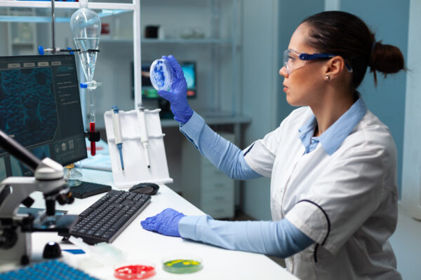 Biologist researcher woman holding transparent petri dish analyzing blue solution